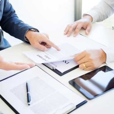 Man signing a car insurance policy, the agent is holding the document